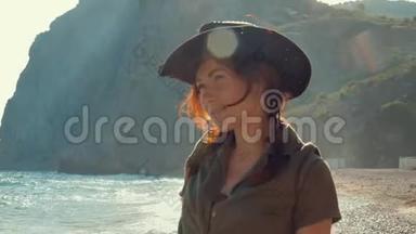 一个美丽的红发旅行女孩戴着牛仔帽在海边的肖像。